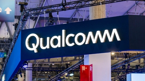 lluminated Qualcomm logo on a large dark blue exhibition stand at a trade show with overhead lighting